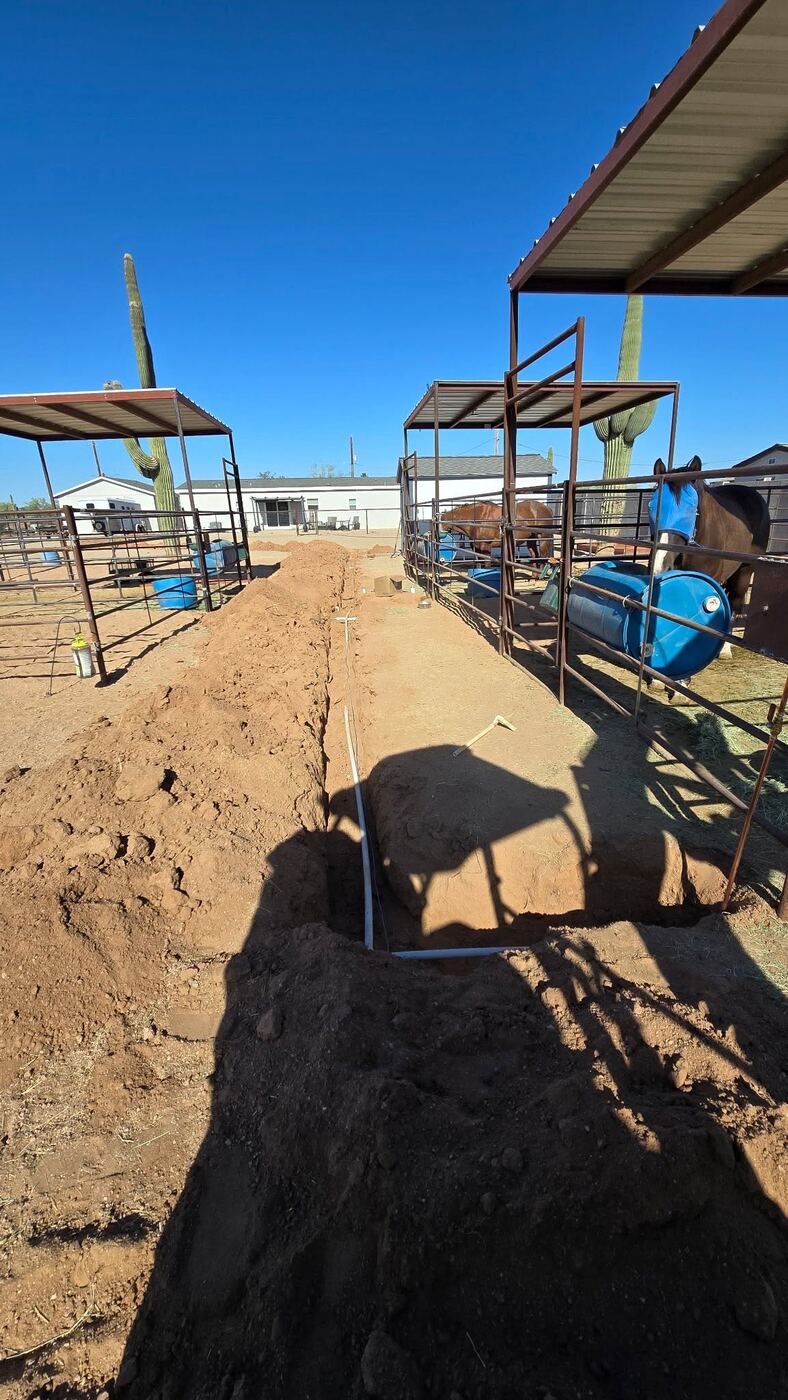 Excavator trenching on ranch property with mountains